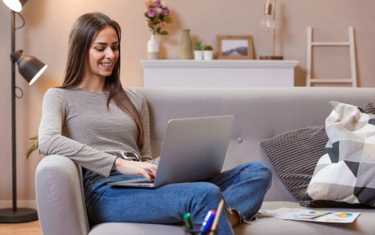 Na imagem, vemos uma mulher sentada confortavelmente em um sofá, com o notebook apoiado em seu colo. Ela busca representar a importância do autoconhecimento para o sucesso profissional.
