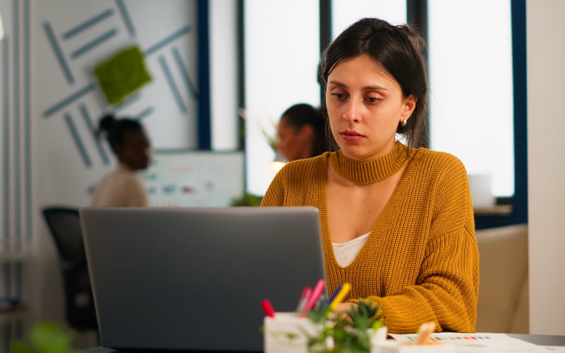 A imagem mostra uma mulher mexendo em um notebook. Ela está com um semblante pensativo e preocupado, refletindo sobre os principais desafios do modelo de trabalho híbrido.