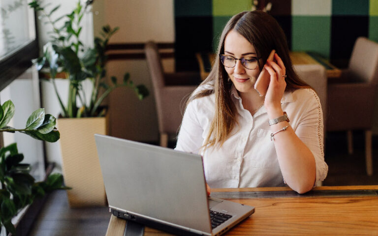 A imagem mostra uma mulher trabalhando em um notebook e conversando ao celular. Ela busca mais informações sobre como adequar sua empresa à Lei Geral de Proteção de Dados (LGPD).