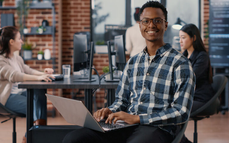 Homem negro em um ambiente descontraído de trabalho. Ele trabalha feliz, por ter a oportunidade de entender como aprimorar o autodesenvolvimento profissional.