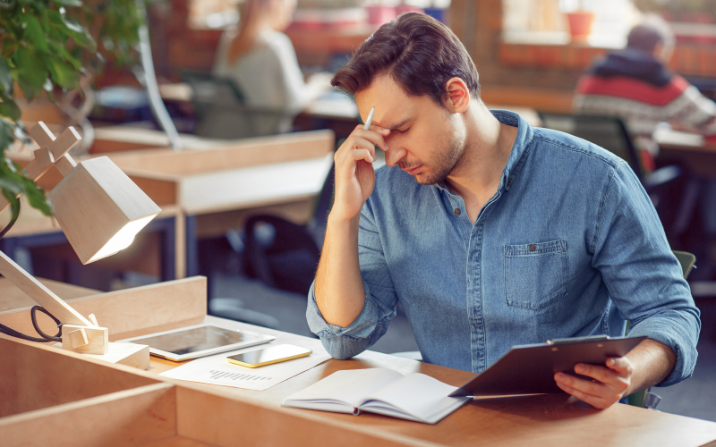 A imagem mostra um homem com semblante tenso e mão apoiada na testa trabalhando em escritório. Ela busca representar o quiet quitting.