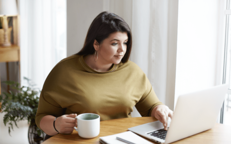 Imagem de capa para artigo sobre Hunting no RH. Na imagem, mostra uma mulher trabalhando em home office à mesa, usando notebook e tomando café em um ambiente claro e aconchegante com luz natural pela janela ao fundo.