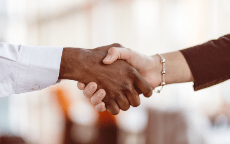 Duas pessoas apertam as mãos em um ambiente corporativo, simbolizando a formalização de um acordo profissional. A imagem ilustra o processo de contratação e os diferentes tipos de contrato de trabalho.