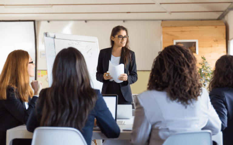 "Líder mulher apresentando para equipe diversa de profissionais em sala de reunião, ilustrando conceito de liderança inclusiva.