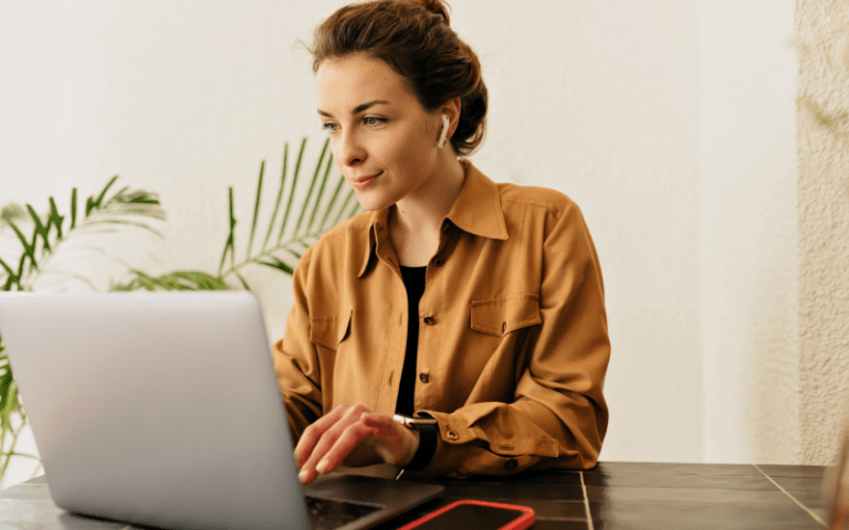 Recrutadora trabalha de forma focada diante de seu notebook, realizando a busca ativa e a triagem de candidatos qualificados. Vestindo uma camisa mostarda e fones de ouvido sem fio, ela exibe uma expressão de atenção e satisfação, representando a eficiência e a estratégia do processo de recrutamento pelo LinkedIn em um ambiente moderno.
