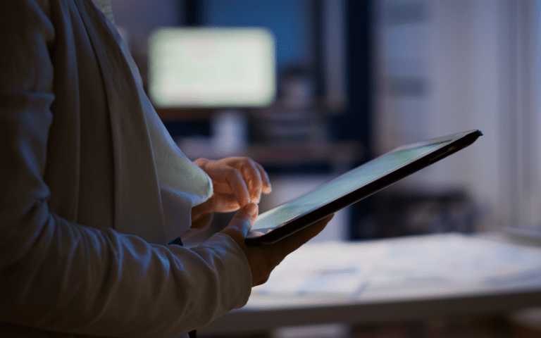Close lateral nas mãos e no perfil de uma profissional de Recursos Humanos que utiliza um tablet para analisar candidatos. A tela iluminada reflete em suas mãos enquanto ela realiza a triagem digital de currículos em um escritório moderno.