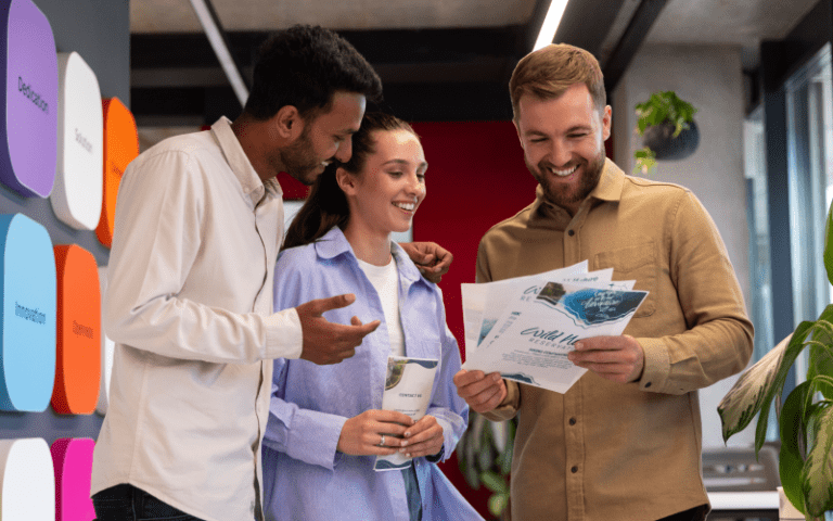 Imagem de capa de artigo sobre Employer Branding, mostrando uma equipe de trabalho sorridente em um ambiente moderno, analisando panfletos e comunicados durante uma reunião ou apresentação, com três pessoas conversando e colaborando