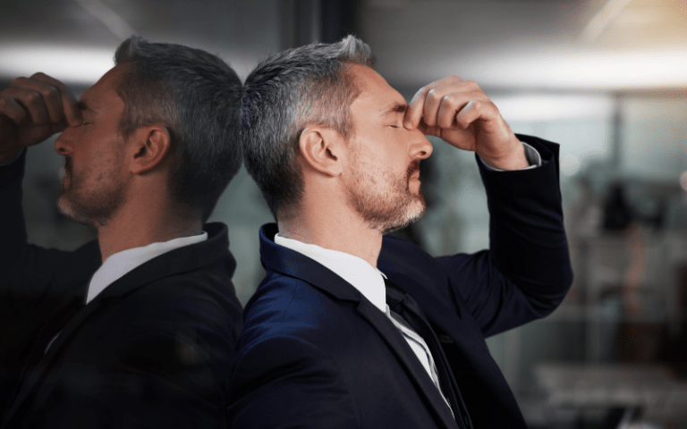 Imagem de capa para artigo sobre liderança ineficaz. Homem em traje corporativo demonstra exaustão ou sobrecarga no ambiente de trabalho, pressionando os olhos fechados em um momento de estresse, com seu reflexo projetado ao fundo.