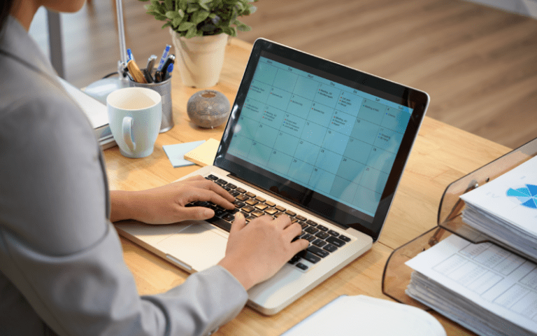 Imagem de capa de um blog post sobre gestão de tempo. Profissional utilizando um notebook com um calendário digital aberto, organizando a agenda em um ambiente de escritório.