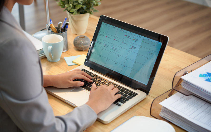 Imagem de capa de um blog post sobre gestão de tempo. Profissional utilizando um notebook com um calendário digital aberto, organizando a agenda em um ambiente de escritório.