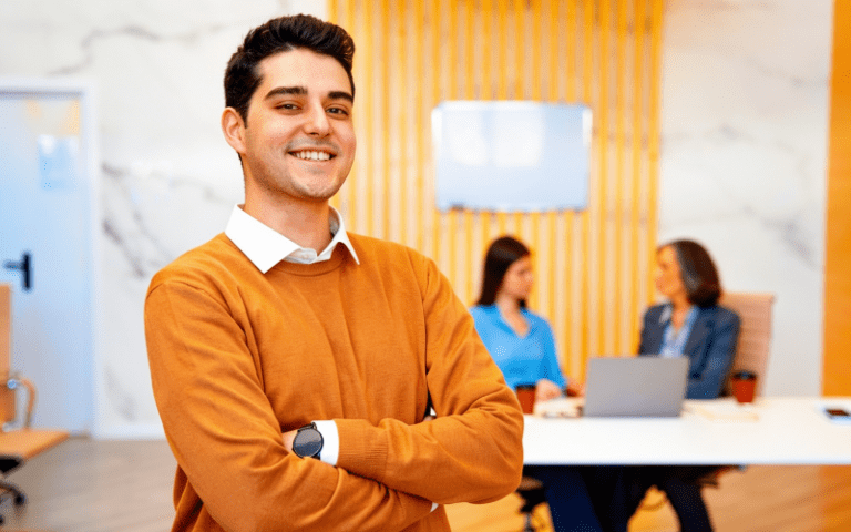 Imagem de capa para artigo sobre direitos dos estagiários, mostrando um estagiário sorridente em ambiente corporativo, com colegas ao fundo em reunião.