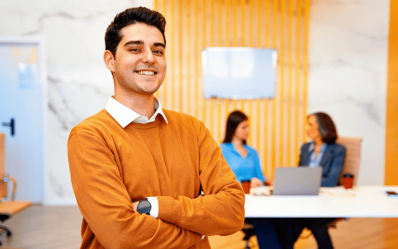 Imagem de capa para artigo sobre direitos dos estagiários, mostrando um estagiário sorridente em ambiente corporativo, com colegas ao fundo em reunião.