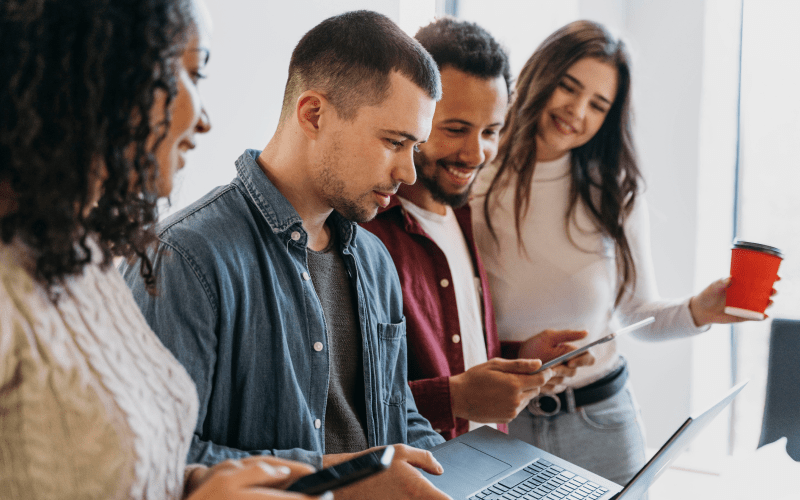 Jovens utilizam notebook e dispositivos móveis em um ambiente corporativo, ilustrando a busca por oportunidades e o processo de candidatura para um estágio remunerado.