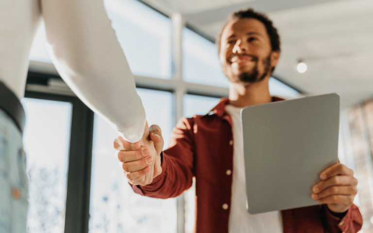 Aperto de mãos em ambiente corporativo simulando conexão entre candidato e recrutador em uma entrevista de emprego.