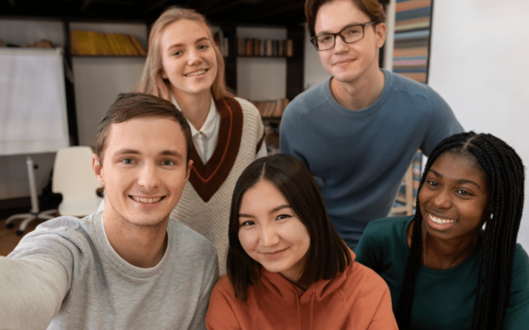 Grupo diversificado de jovens sorridentes em destaque. Ao fundo, um ambiente de trabalho ou reunião. Imagem usada para ilustrar um conteúdo sobre férias de estagiário, publicado no Blog da Selpe.