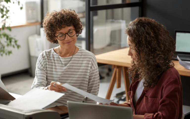 Mentora orientando uma profissional em ambiente de trabalho, simbolizando a troca de experiências e o desenvolvimento de talentos por meio do mentoring corporativo.