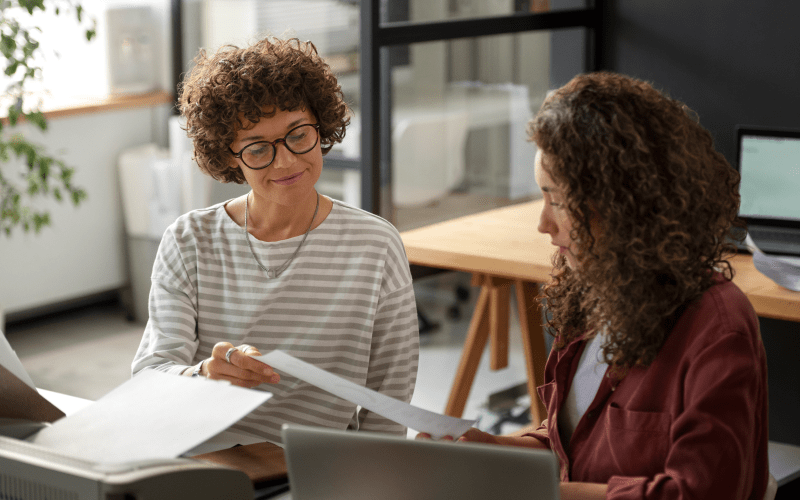 Mentora orientando uma profissional em ambiente de trabalho, simbolizando a troca de experiências e o desenvolvimento de talentos por meio do mentoring corporativo.