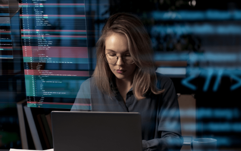 Na imagem, uma mulher com óculos trabalha concentrada em um laptop. Linhas de código sobrepostas simbolizam a análise e a segurança de dados no ambiente corporativo.