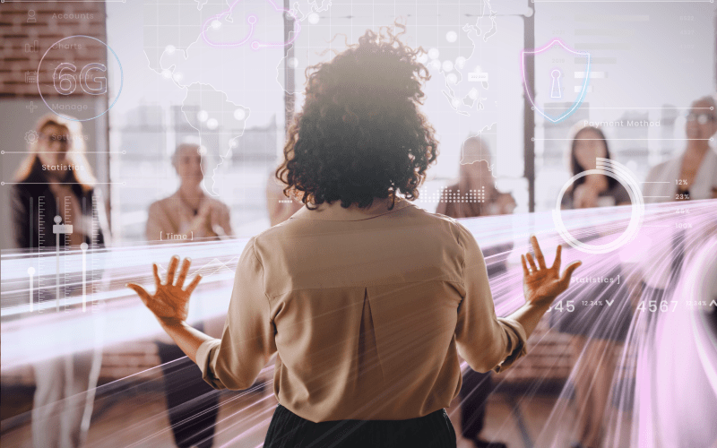 Profissional de costas reunida com um grupo, diante de gráficos digitais e elementos tecnológicos que representam análise de competências, uso de dados e processos de contratação e desenvolvimento baseados em habilidades.
