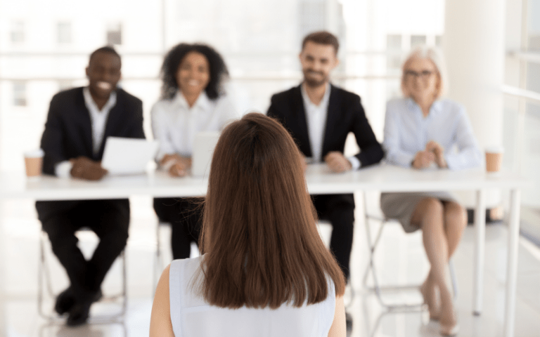Candidata sentada de frente para quatro recrutadores durante uma entrevista de emprego em um ambiente corporativo, representando uma etapa do processo seletivo.