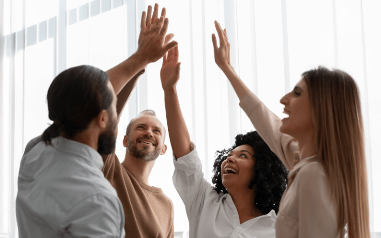 Quatro profissionais celebram juntos com um high-five coletivo, simbolizando união, entusiasmo e o impacto positivo da liderança de alta performance nas equipes.