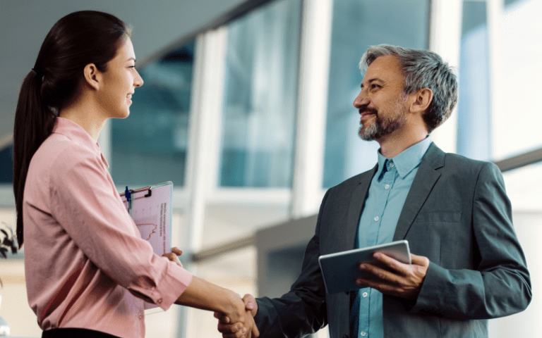 Profissionais em ambiente corporativo apertam as mãos, simbolizando transição e sucessão de liderança nas organizações.